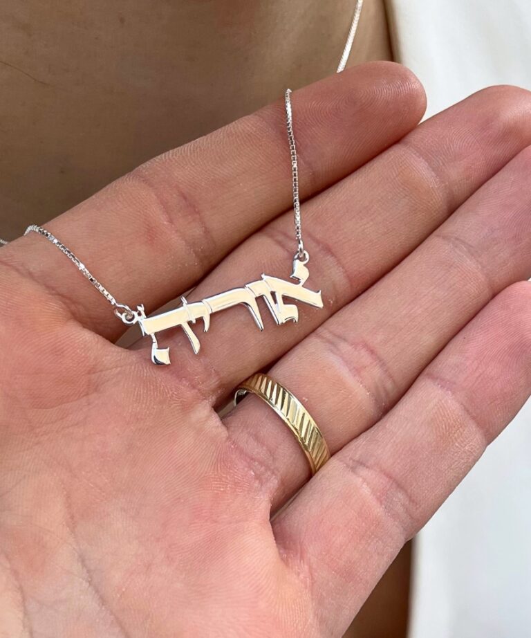 Delicate name pendant resting on a hand with gold ring