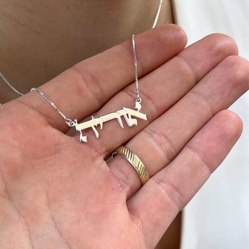 Delicate name pendant resting on a hand with gold ring