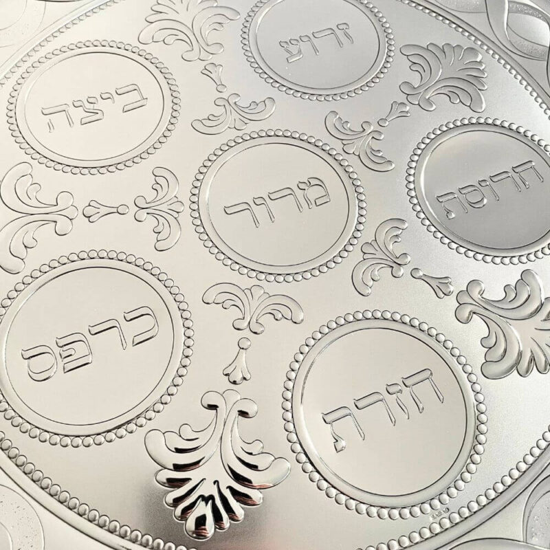 Detailed view of all six engraved Passover food labels on the silver Seder plate