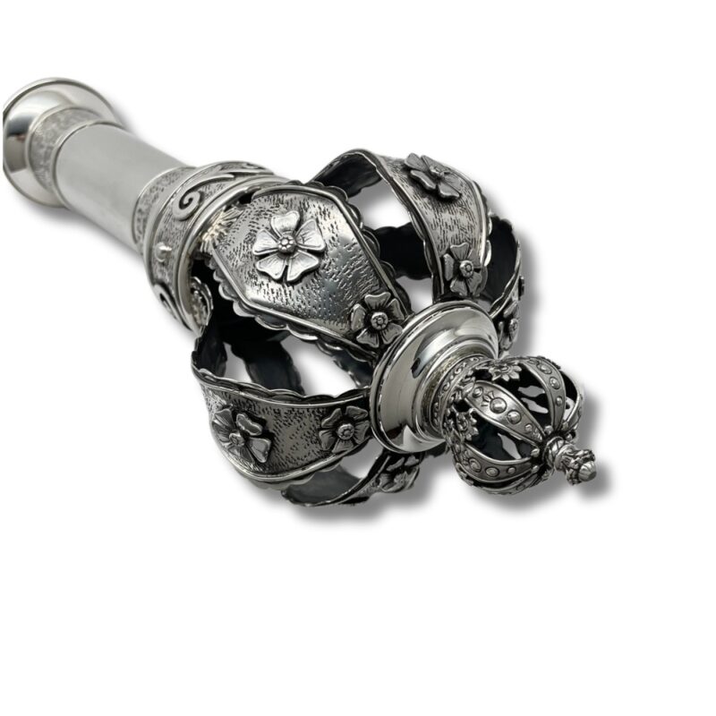 Detailed close-up of a silver Torah finial crown, showcasing raised floral engravings and curved design