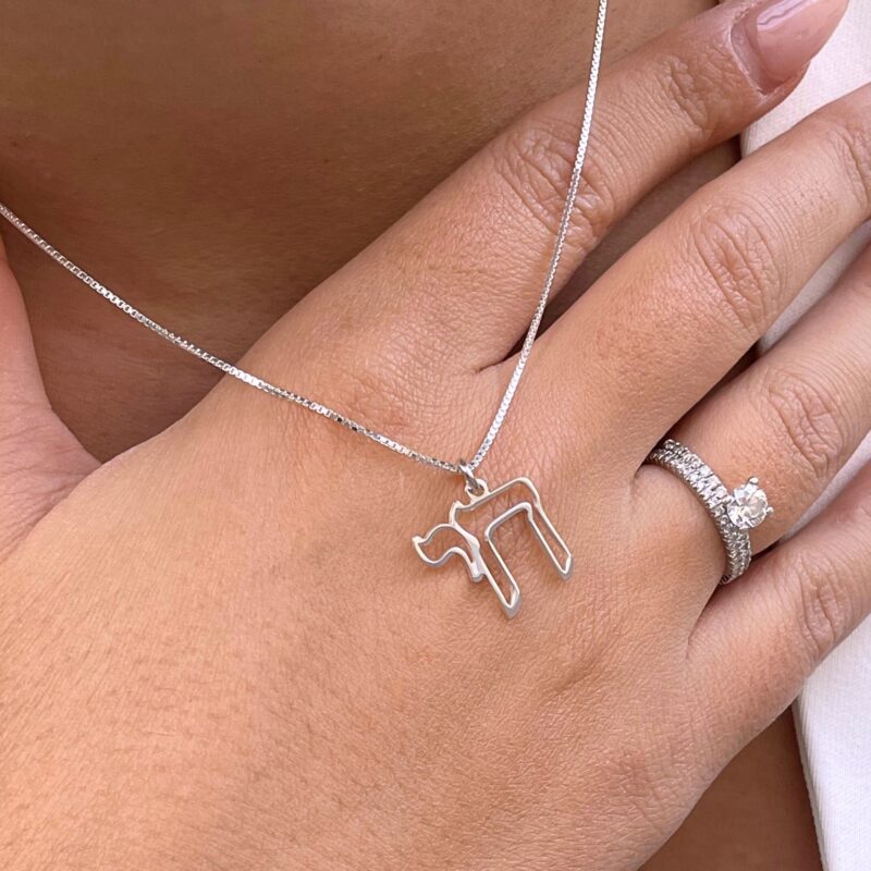 Jewish Chai necklace in white gold shown on hand with engagement ring